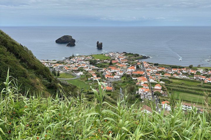 Coastal town with orange rooftops, lush greenery, islands, and cloudy sky.