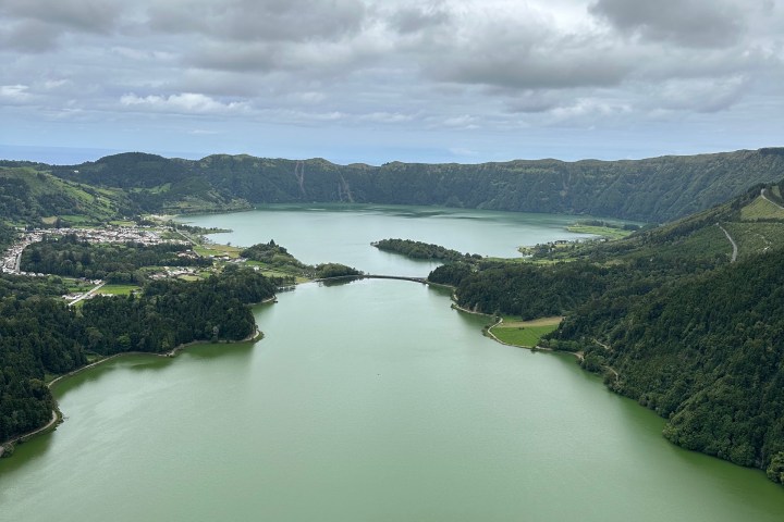 Scenic view of a green lake surrounded by hills under a cloudy sky.