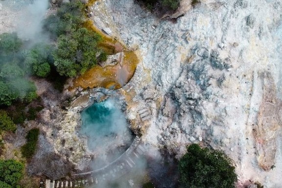 Aerial view of a geothermal landscape with steam, rocks, and vegetation.