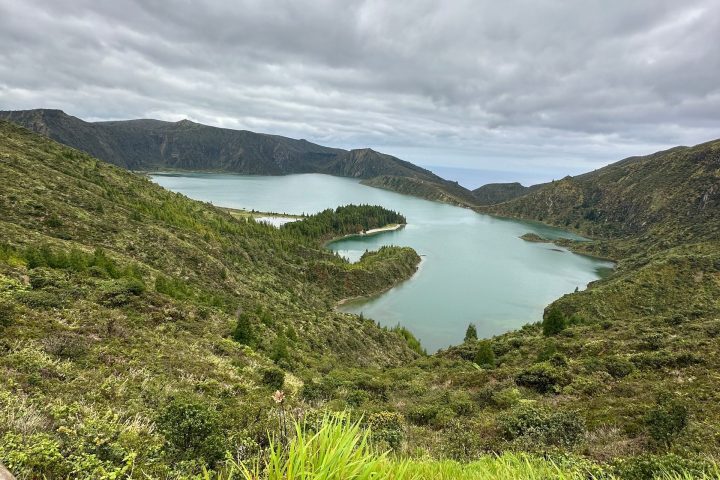 Scenic view of a green landscape with a lake under a cloudy sky.