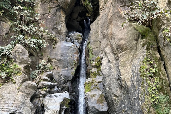 A narrow waterfall cascading down a rocky cliff into a small pool with a swimmer.