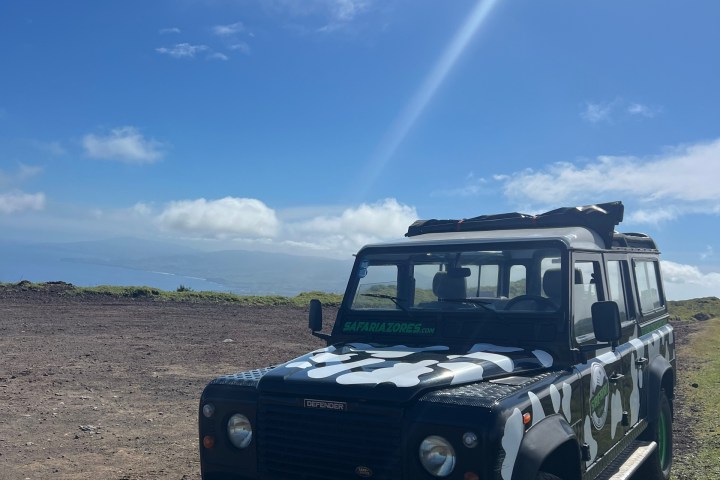 Black and white safari Land Rover on a dirt road under a blue sky with clouds.