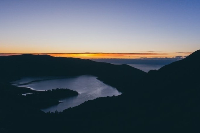 Sunset over a dark silhouette of hills and a lake under a clear sky.