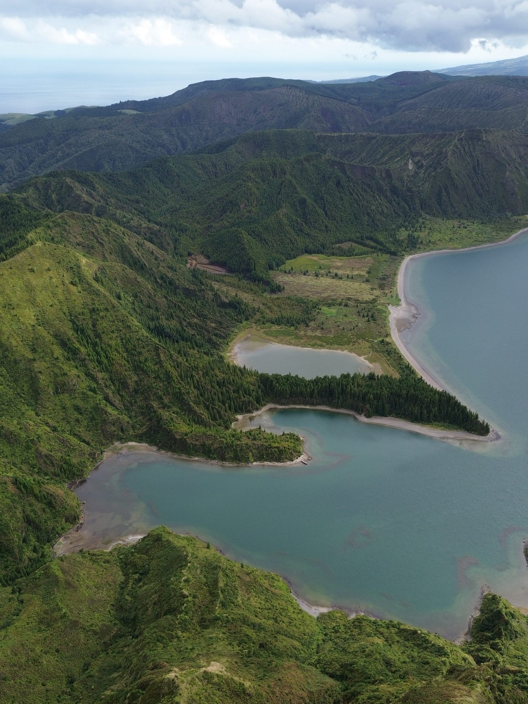 Aerial view of a mountainous landscape with green hills surrounding a lake under cloudy skies.