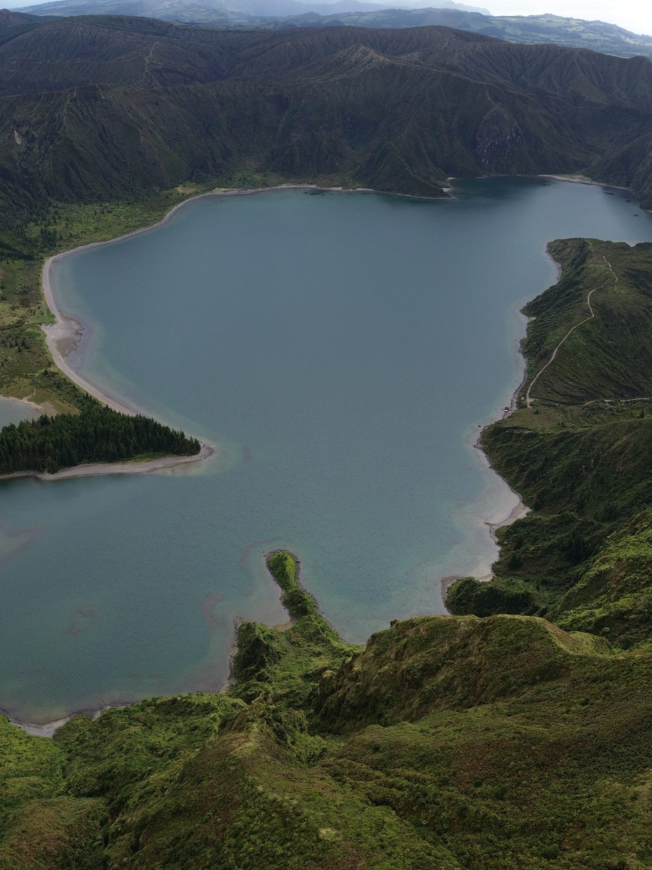 Aerial view of a lake surrounded by green hills under a cloudy sky.