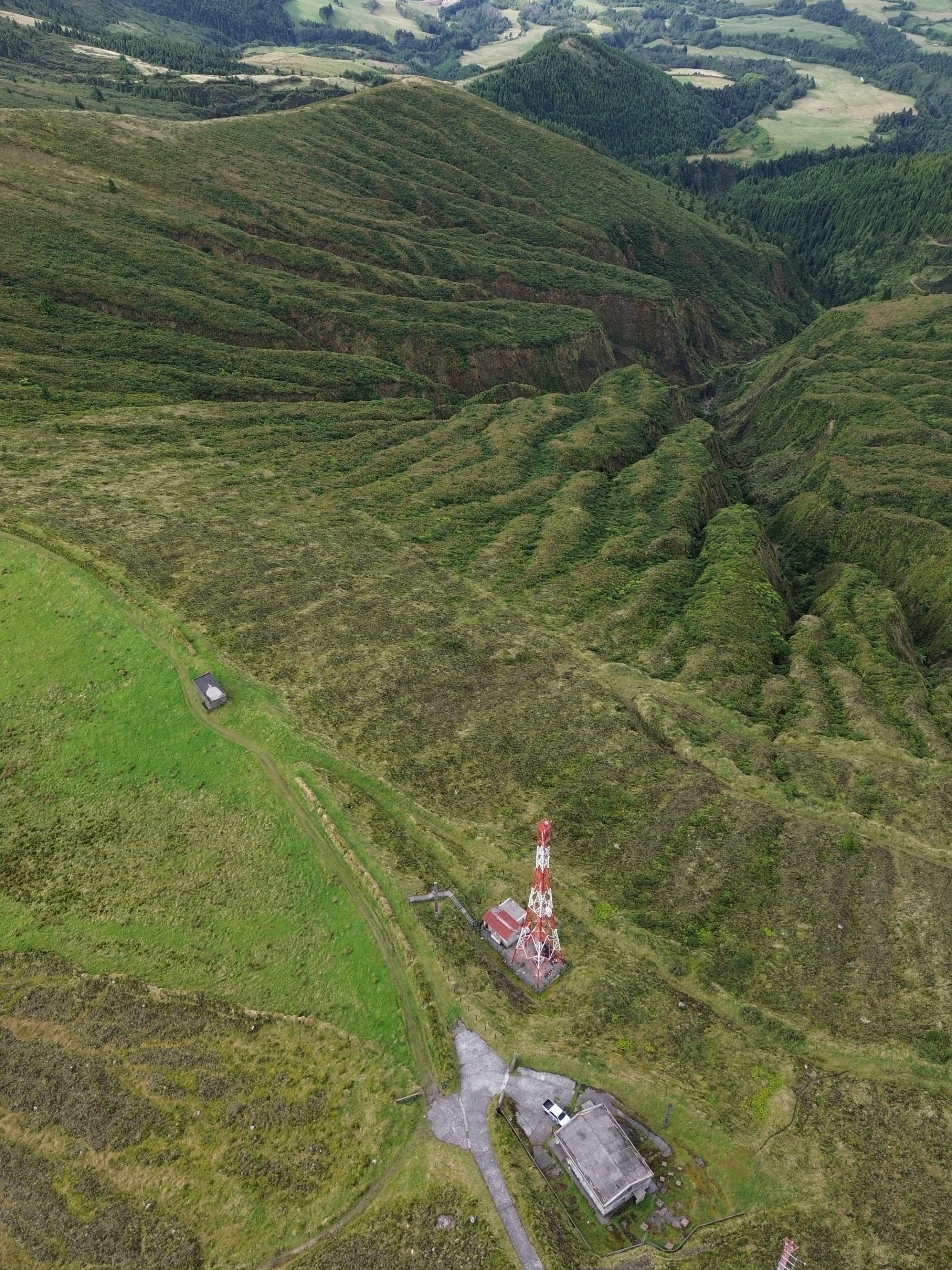 Aerial view of hilly landscape, tower, and buildings, coastline in distance.