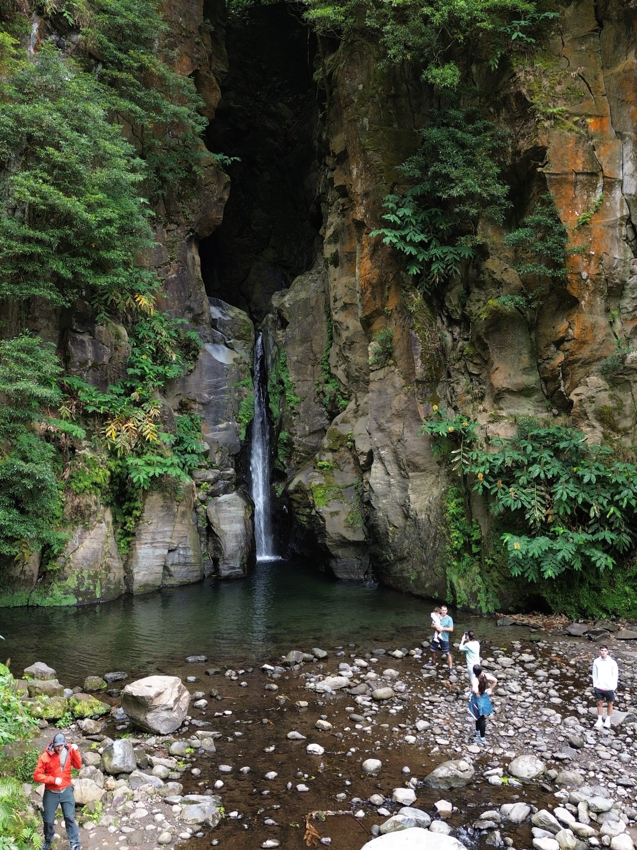 People exploring rocky waterfall area with lush green foliage.