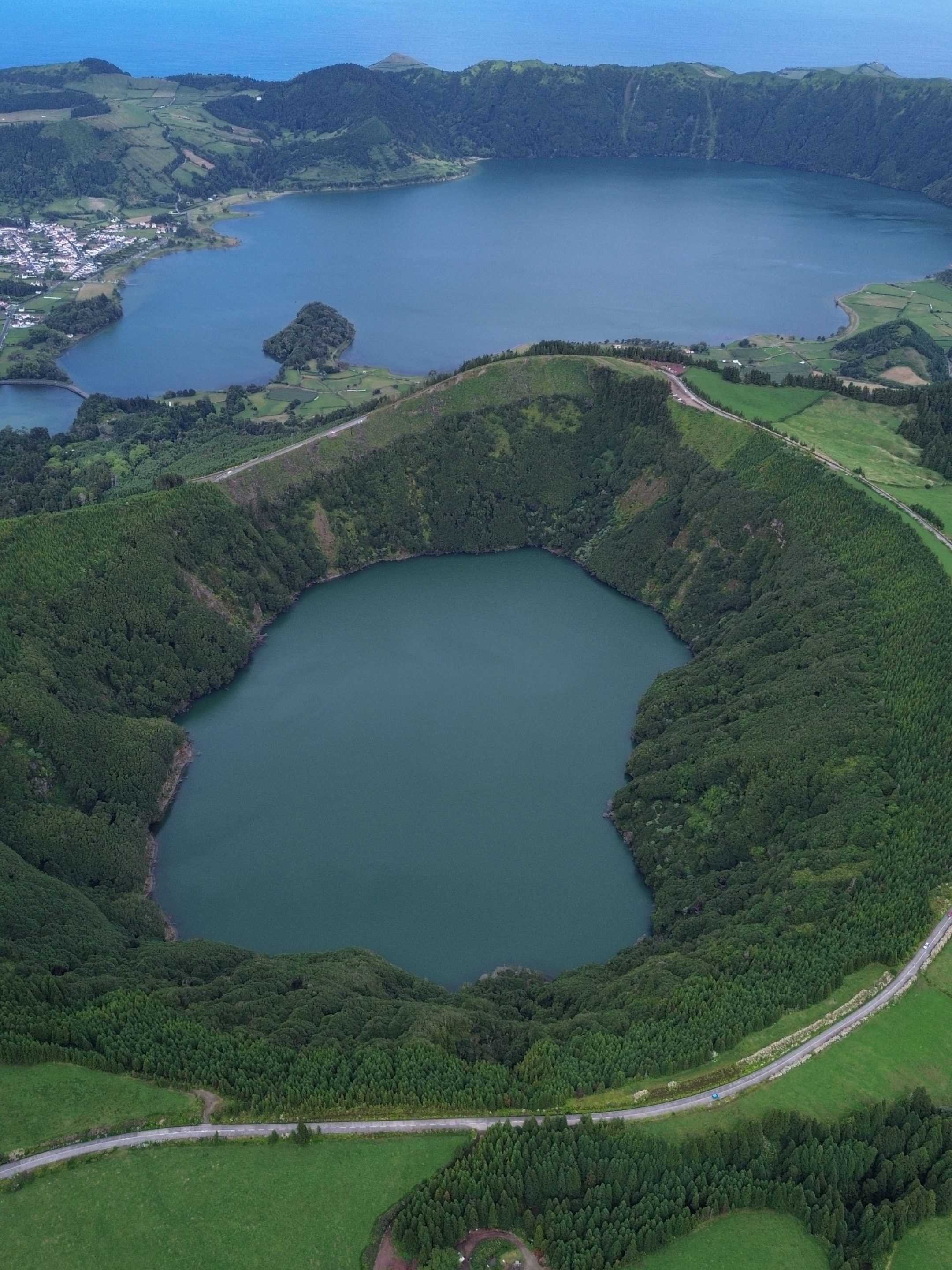 Aerial view of two crater lakes surrounded by lush greenery and distant ocean horizon.
