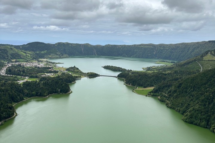 Aerial view of a large, greenish lake surrounded by hills and overcast skies.