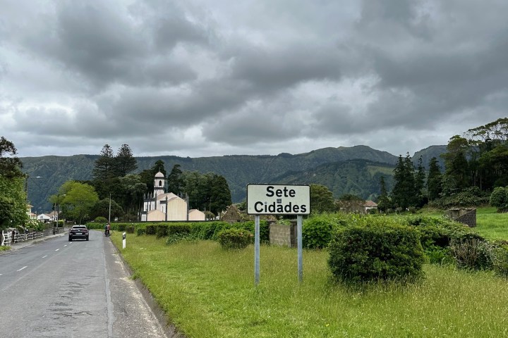 Roadside view with 'Sete Cidades' sign, church ahead, cloudy sky above.